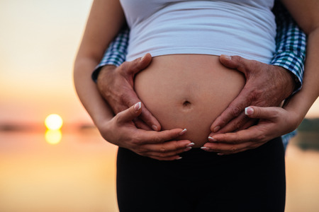 Man holding woman's pregnant belly outdoors on a sunset.の写真素材