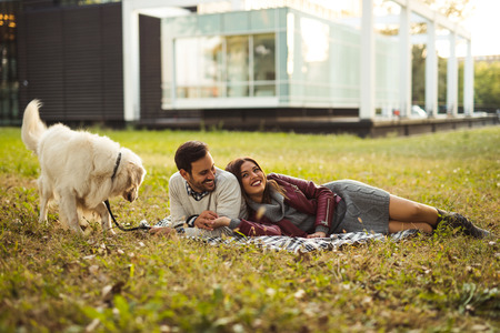 Happy couple lying with their dog on the grass in the park.の写真素材