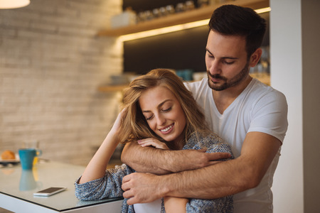 Beautiful couple enjoying a hug at home in the kitchen.の写真素材