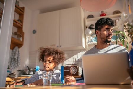 Man working on a computer while his daughter is drawing.の写真素材