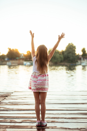Rear view of a girl raising her hands towards the sun.の写真素材