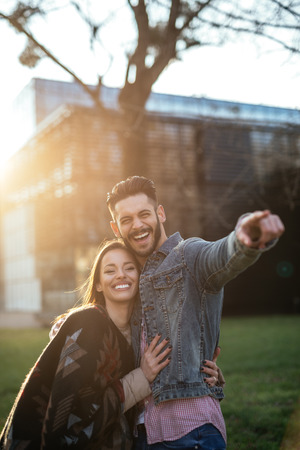 Portrait of a couple hugging each other while the man is pointing in the distance at sunset.の写真素材