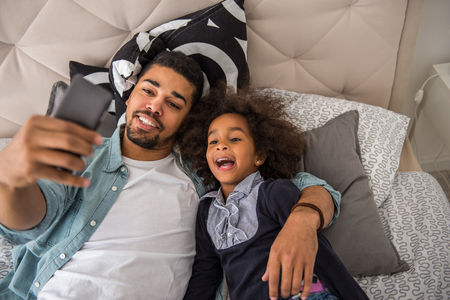 Cute african american girl making selfie with dad.の写真素材