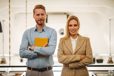 Portrait of two business partners. Both are standing with arms crossed and ready for new challenges. Man is holding a yellow notebook.の写真素材