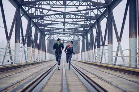 Shot of an athletic couple running on the train bridge during morning workout.の写真素材