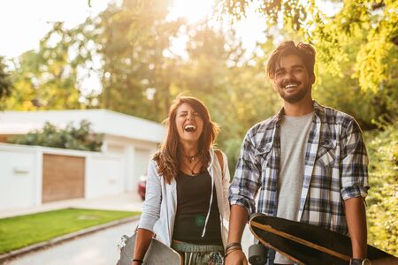 Portrait of a laughing skateboarding couple having a good time at sunset in the city.の写真素材