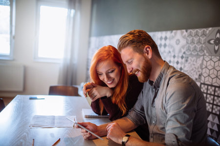 Photo of two happy friends working from home on a digital tablet.