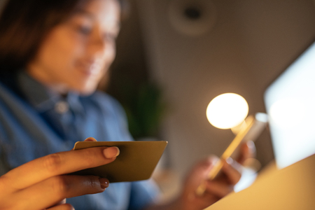 Young female holding a credit card and using mobile phone in the evening.の写真素材