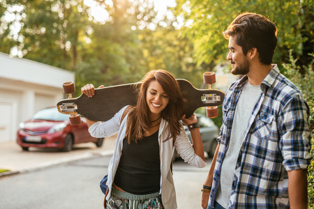 Shot of a young couple walking down the street and carrying a long board.の写真素材