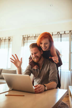 Photo of happy couple enjoying spending time together while connecting to friends over laptop.の写真素材