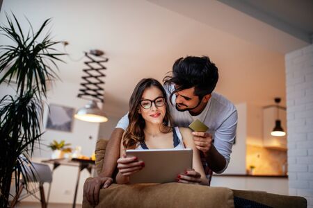 Photo of a smiling young couple shopping online on a digital tablet at home.の写真素材