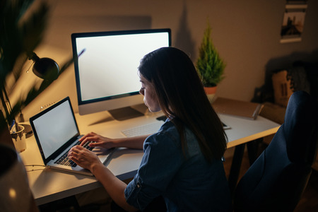 Rear view of a woman working on a computer at home.の写真素材