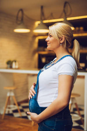 Portrait of a beautiful pregnant woman standing in the kitchen.の写真素材