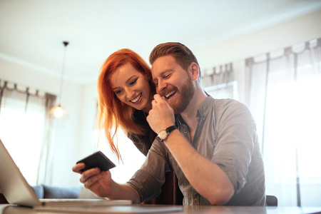 Relaxed young couple using a mobile phone and having fun at home.の写真素材