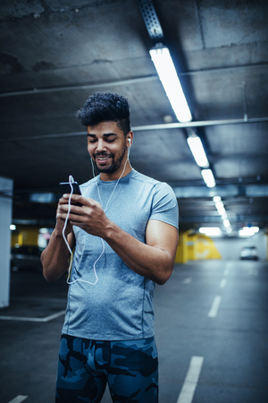 Shot of african american athlete man using mobile phone and listening to the music in the underground car parking.の写真素材