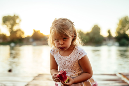 Close up portrait of a young beautiful girl eating a slice of watermelon at sunset.の写真素材
