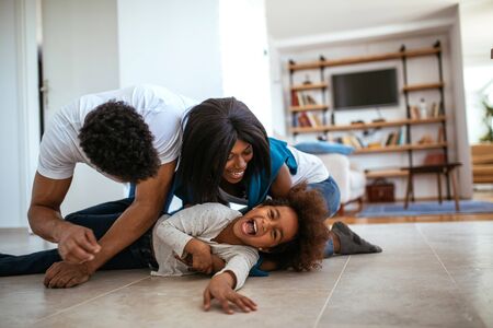 Happy african american parents enjoying playing with daughter at home.の写真素材