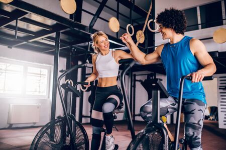 Photo of smiling young couple exercising together on an assault air bike in the gym.の写真素材