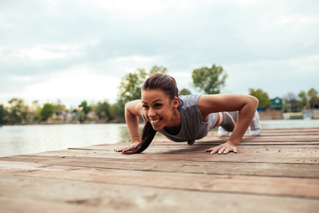 Satisfied young athlete woman doing push ups outdoors.の写真素材