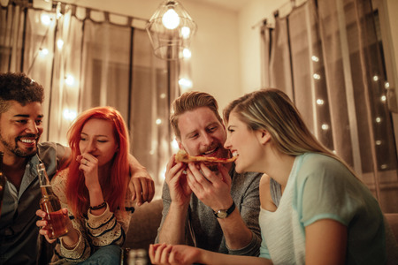 Portrait of friends enjoying eating pizza together and drinking beer at home.の写真素材