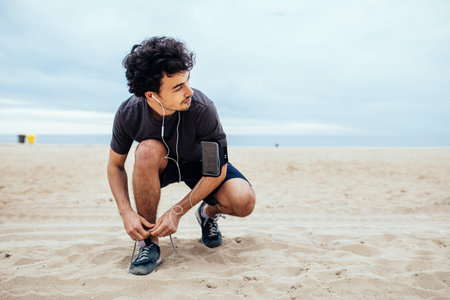 Handsome man tying a shoe lace while running on the beach.