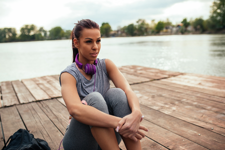 Beautiful young sporty woman sitting next to lake.の写真素材