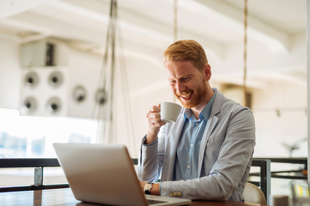 Portrait of a business man drinking coffee while working on a laptop.の写真素材