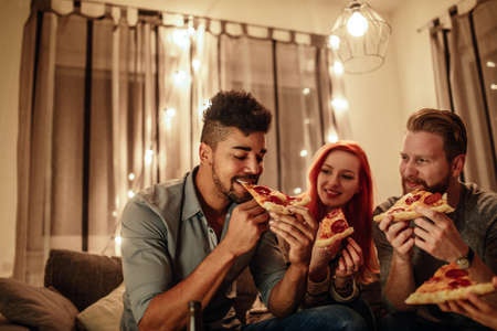 Portrait of a young male eating pizza with friends.の写真素材