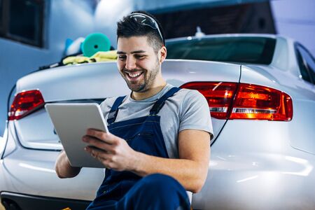 Portrait of a smiling young auto mechanic using digital tablet while leaned on the car.の写真素材