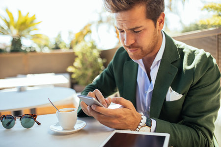 Handsome and elegant man using a mobile phone and enjoying a coffee time.