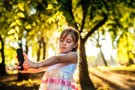 Young girl taking a photo of herself in the park at sunset.の写真素材