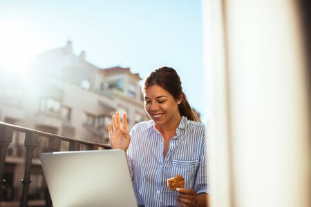 Beautiful woman making a video call while having snack on a balcony.の写真素材