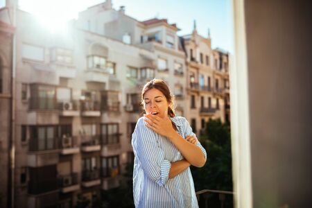 Portrait of a young woman yawning on the balcony early in the morning.の写真素材