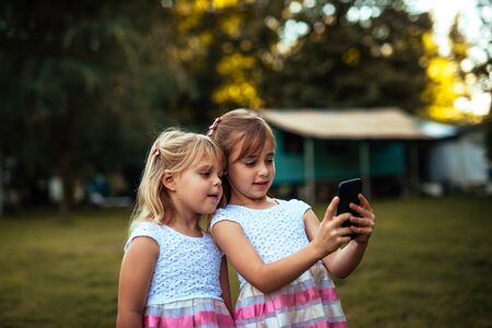 Shot of two blonde sisters posing for a picture on the mobile phone outdoors.の写真素材