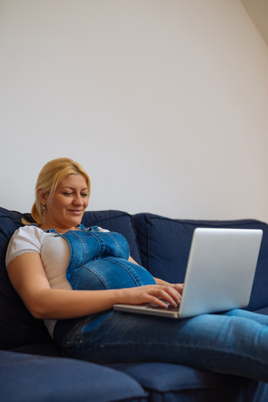 Photo of a pregnant woman lying on the sofa and using laptop.の写真素材