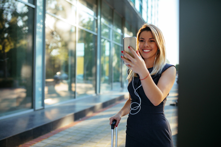 Shot of a lovely young business woman standing at the airport and using mobile phone.の写真素材