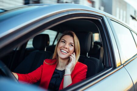 Shot of a smiling successful young business woman sitting in the car and talking on the mobile phone.の写真素材