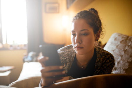 Portrait of a young teenage woman using mobile phone while lying in the bed.の写真素材
