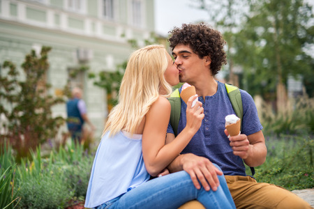 Portrait of a young couple eating ice cream and kissing outdoors.の写真素材