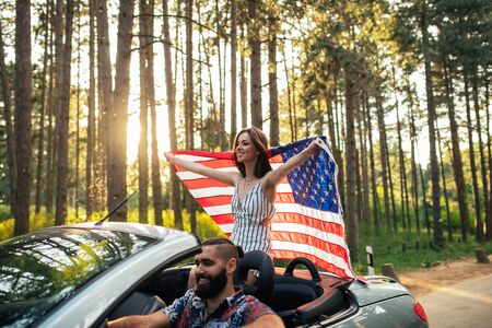 Shot of a young woman holding an american flag while riding in a car.の写真素材