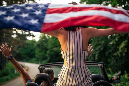 Photo of a young woman spreading an american flag in the car.の写真素材