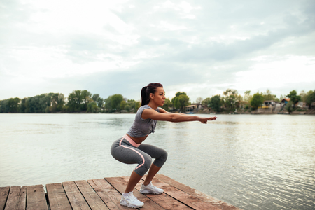 Portrait of an athlete woman doing squats outdoors by the lake.の写真素材