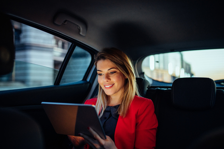 Close up portrait of a young business woman using digital tablet in the back seat of the car.の写真素材