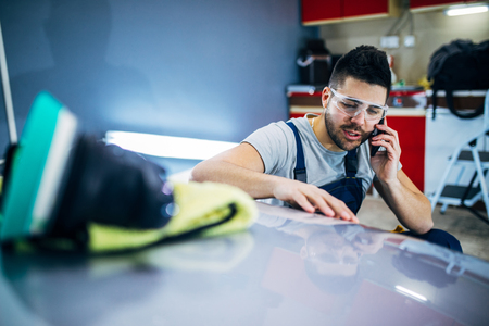 Man talking on the phone while doing car polish in his workshop.の写真素材