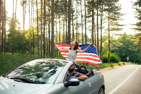 Shot of a young girl holding an american flag while sitting in the car.の写真素材