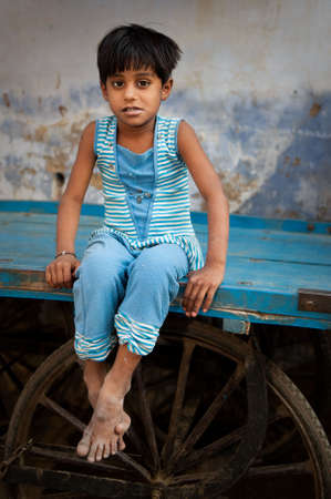 A young indian girl sitting on a cart looking shyly at the camera.のeditorial素材