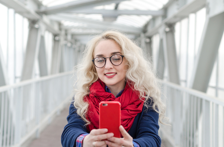 Beautiful blonde girl in blue coat and red scarf taking selfie photo at the airportの写真素材