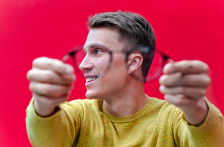 Young man with eyesight problem, threw glasses and smiling on red backgroundの写真素材