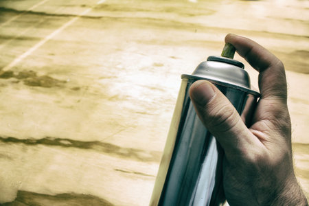 Photograph of a spray paint can and a human hand on a wood table