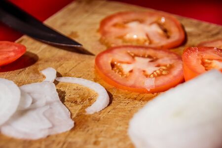 Photograph of a knife, tomato slices and onion on a wood cutting boardの写真素材
